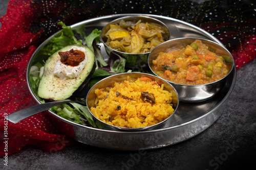 Indian food platter with serving bowls: mixed veggetable curry, cabbage curry, rice pilaf, salad and avocado photo