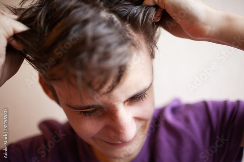 Teen guy squeezes his head and screams and grimaces on a light background