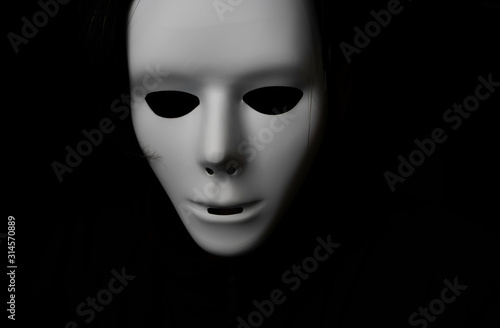 Scary white mask in the dark. Spooky guy in white masquerade. Black, invisible eyes. Black hair. Halloween style. 
