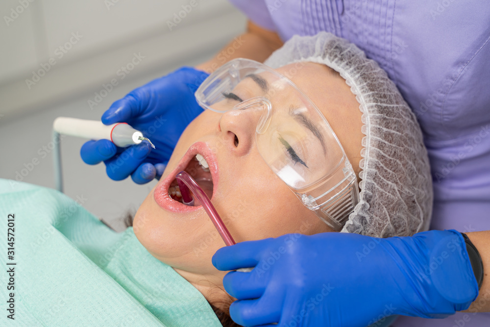 Naklejka premium Close-up of a girl’s patient at the moment when the dentist is using a saliva ejector to clean the oral cavity during the process of calculus removal.