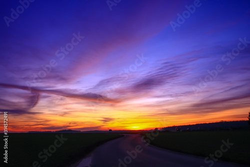 Beautiful multicolored sunset. Cumulonimbus and very colorful stratus in a dramatic sky. Sun disappearing behind a hill.