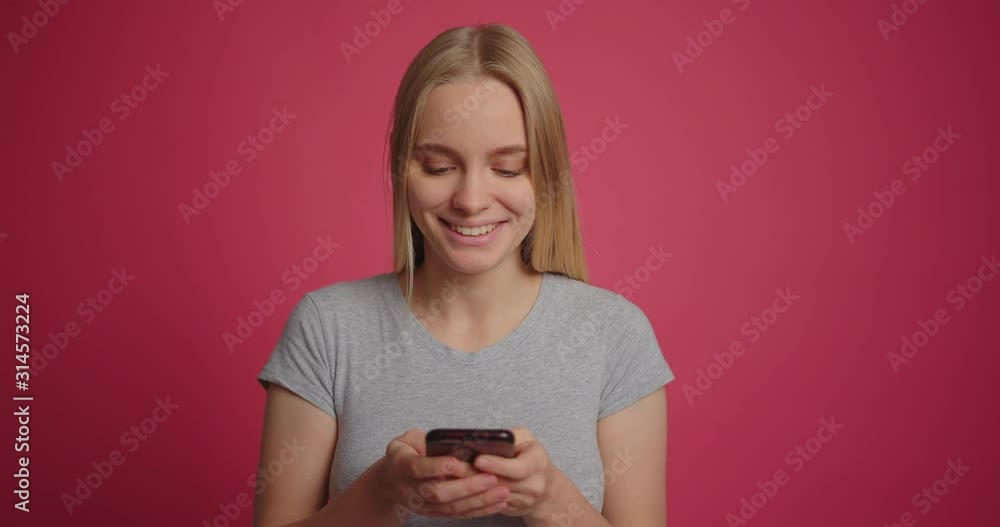 Blonde girl flirting and chating on smartphone at pink wall backdrop slow motion Blonde girl flirting and chating on smartphone at pink wall backdrop slow motion
