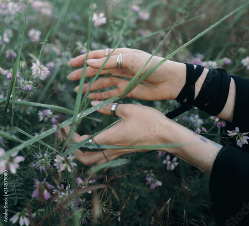 Female hands with rings touch the grass and flowers.