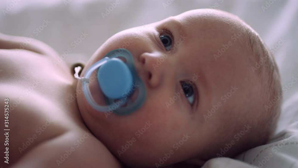 Caucasian baby looks into camera, then looks up while sucking on pacifier Caucasian baby looks into camera, then looks up while sucking on pacifier