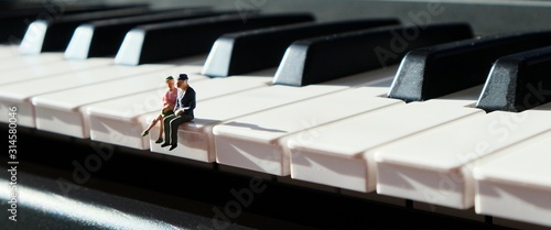 Photography Miniature figurines of an elderly couple, sitting together on the keys of a piano