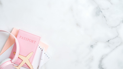 Summer vacation and travel concept. Flat lay design with airplane, pink passport, paper notepad, headphones on marble background. Top view with copy space.
