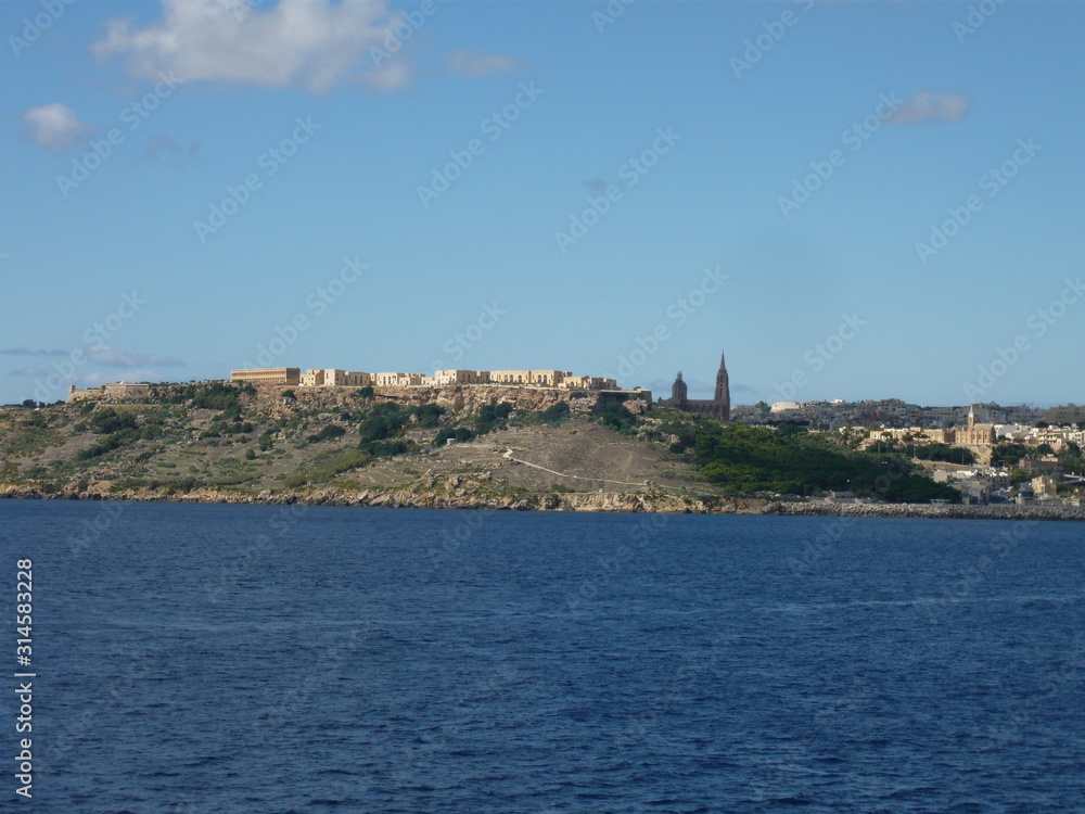 Gozo skyline from ferry with church of The Madonna of Lourdes,  Ghajnsielem Parish Church, apartments, and steep path to sea 