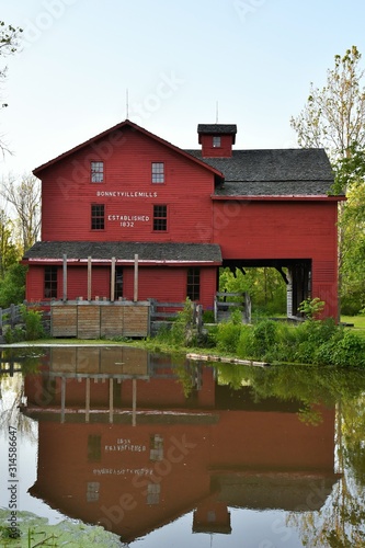 Daytime photo of the red barn mill at Bonneyville Mills in Bristol, Indiana with a calm pond and reflection in the foreground