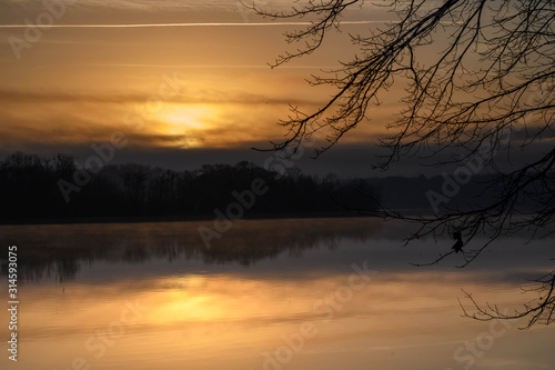 Looking through the trees at the calm river. The clouds are turning orange in the morning sun. © Rick