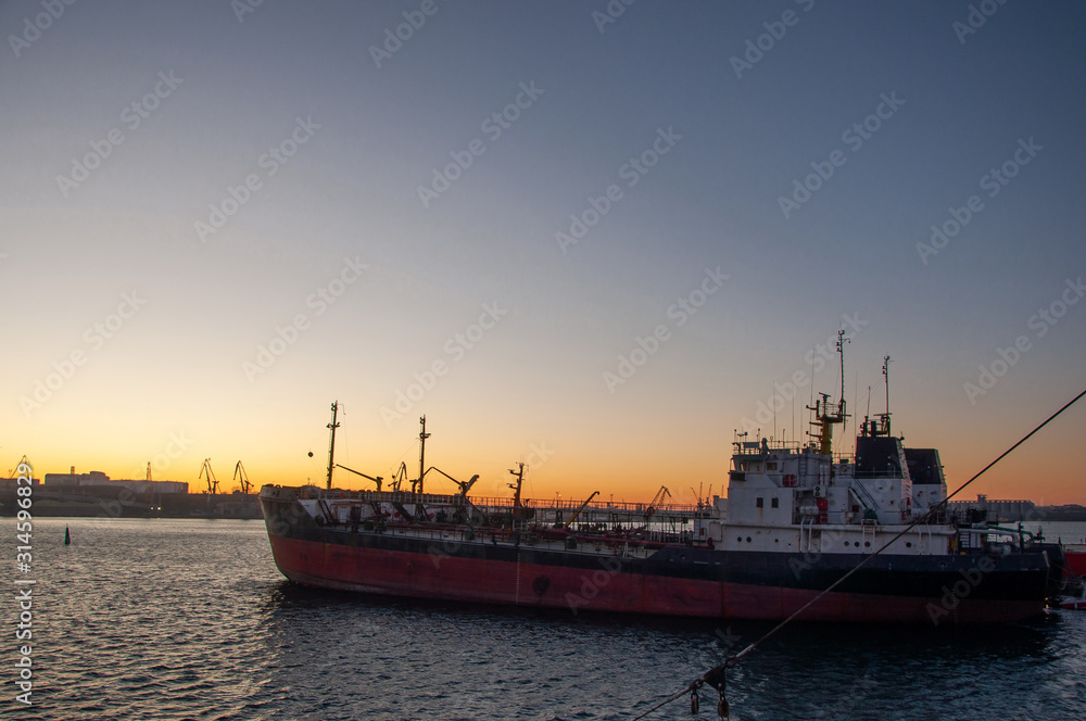 A large old ship with pipes on the deck is empty in the creek of the sea at sunset.