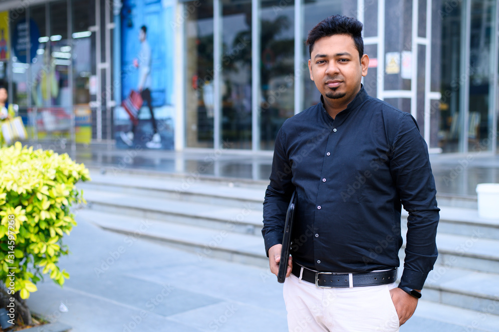 Young entrepreneur or businessman standing near office building with a laptop in hand Young entrepreneur or businessman standing near office building with a laptop in hand