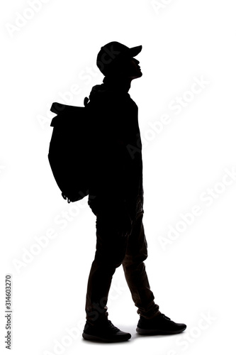 Silhouette of a man wearing a backpack looking like a traveler or hiker trekking.  He is patiently standing and waiting