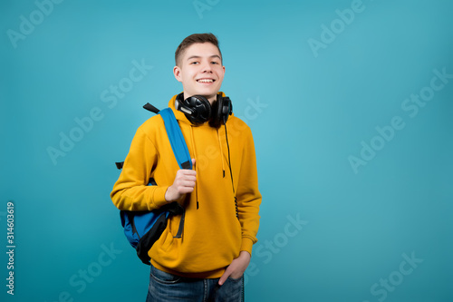 guy with headphones in a yellow sweatshirt on a blue background with a backpack