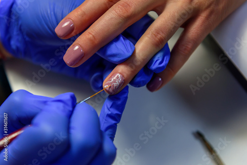 Covering the nails with gel polish  drawing picture on the nail plate. Manicurist in blue gloves apply varnish with a thin brush. Manicure in pastel colors.