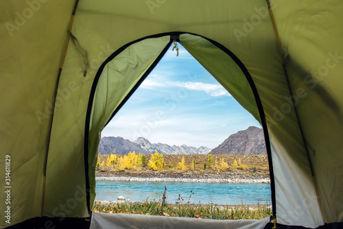 View from the tourist tent on beautiful landscape with turquoise river and high mountains under blue sky. Camping at mountain. Inside the green tent, copy space.