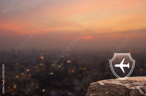 Airplane with shield flat icon on rock mountain over blur of cityscape on warm light sundown, Business travel insurance and safety concept