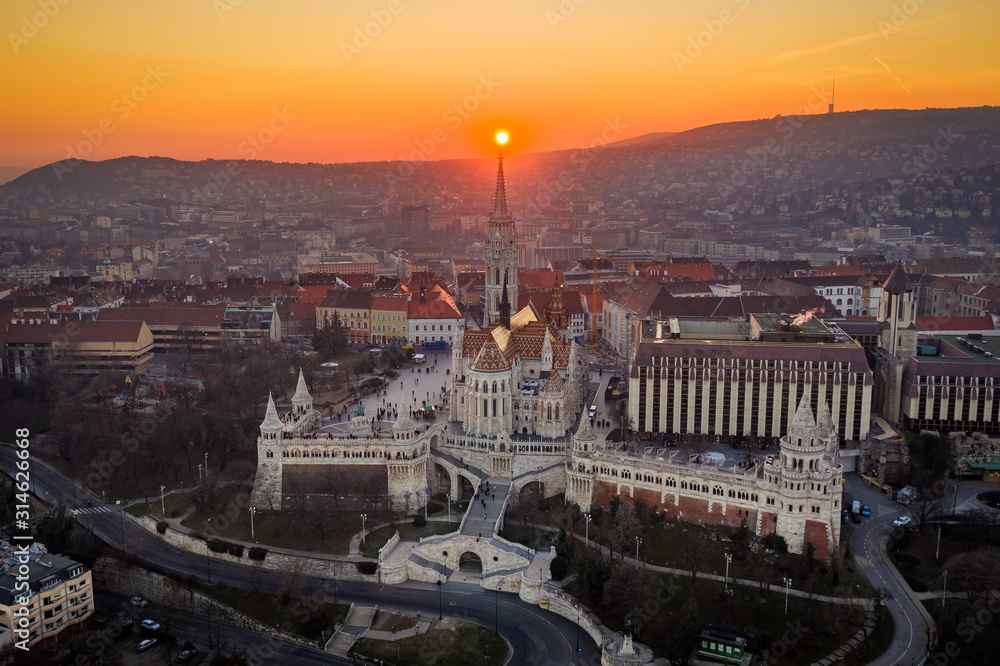 Budapest, Hungary - Aerial view of the famous Fisherman's Bastion (Halaszbastya) and Matthias Chruch at sunset with the sun right behind the church tower. Golden sky at winter time