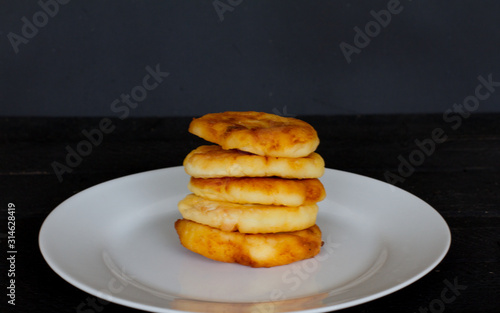 stack of pancakes on a black background. white plate with cheesecakes. breakfast.  the concept of the menu and cooking. five cheesecakes. delicious snack. pastry. space for text.