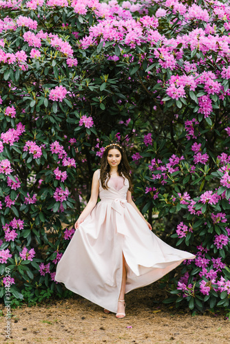 A girl in a long developing dress in the colors of rhododendron walks in the Park