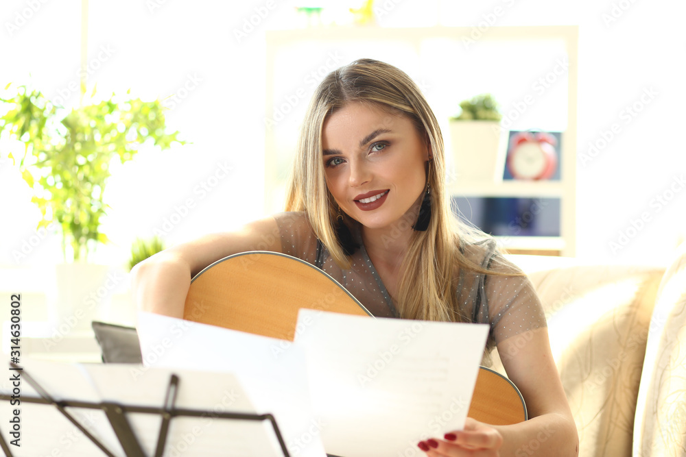 Acoustic Guitar Playing Hobby Workshop at Home. Beautiful Caucasian Woman Music Composer. Blonde with Makeup Looking at Camera. Notes on Music Stand infront. Concert Musical Performance Rehearsal Acoustic Guitar Playing Hobby Workshop at Home. Beautiful Caucasian Woman Music Composer. Blonde with Makeup Looking at Camera. Notes on Music Stand infront. Concert Musical Performance Rehearsal