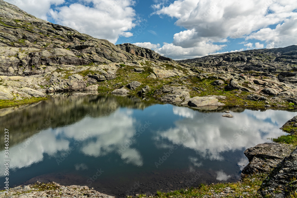 Fototapeta premium Lake landscape with clouds reflection, rocky mountain tundra, way to Trolltunga rock, Norway.