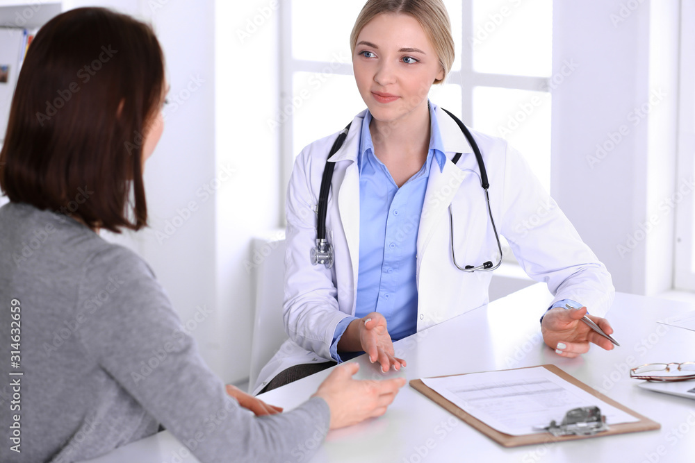 Young woman doctor and patient at medical examination at hospital office. Blue color blouse of therapist looks good. Medicine and healthcare concept Young woman doctor and patient at medical examination at hospital office. Blue color blouse of therapist looks good. Medicine and healthcare concept