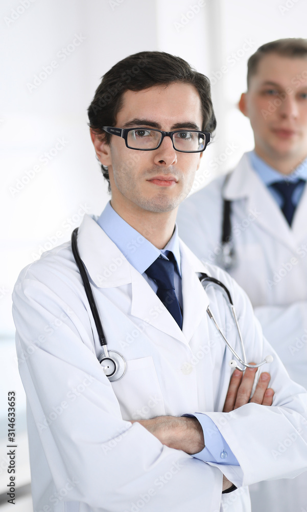Doctor man standing straight with colleague at background. Group of doctors. Perfect medical service in clinic. Medicine and healthcare concepts Doctor man standing straight with colleague at background. Group of doctors. Perfect medical service in clinic. Medicine and healthcare concepts