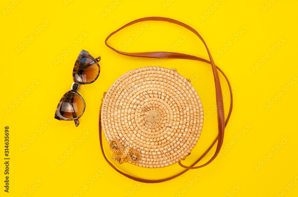 Obraz premium Top view female summer fashion straw round bag and sunglasses on a yellow table background