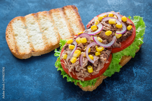 healthy tuna sandwich with grilled bread tomatoes lettuce corn onion on dark blue background