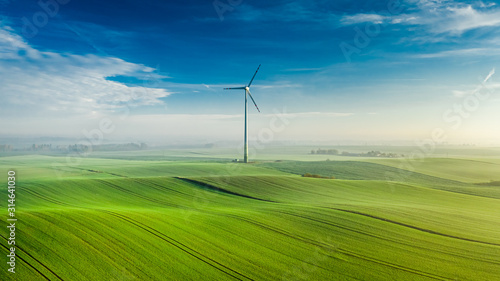 Wind turbine on green field at sunrise, view from above