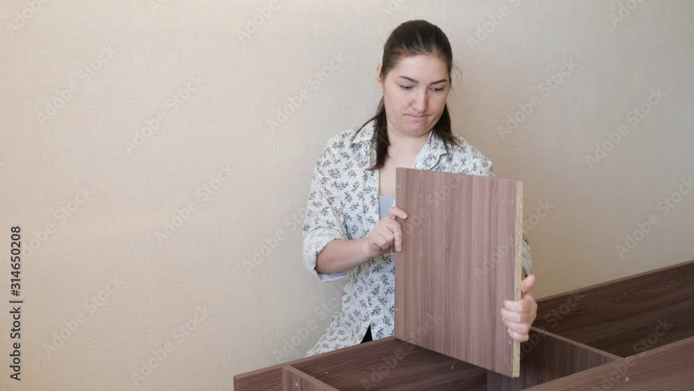 brunette girl in home clothes sits on kitchen floor and tries to assemble prefabricated wooden cupboard parts brunette girl in home clothes sits on kitchen floor and tries to assemble prefabricated wooden cupboard parts