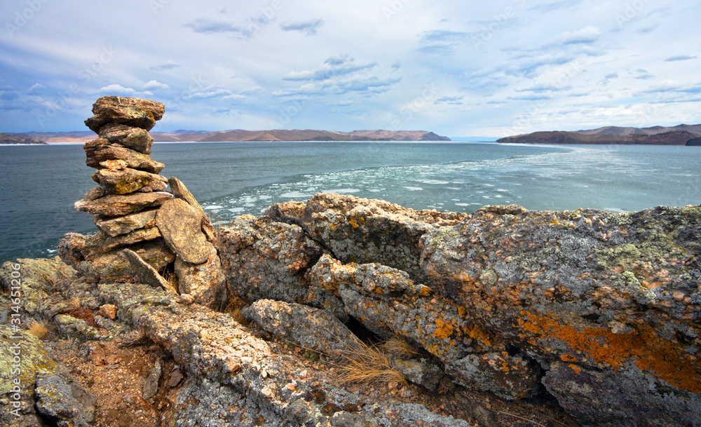 Baikal Lake in spring. Top view of the ice drift in the Olkhon Gate Strait from cape Ulan. Stone pyramids at the top of the cliff - local traditions