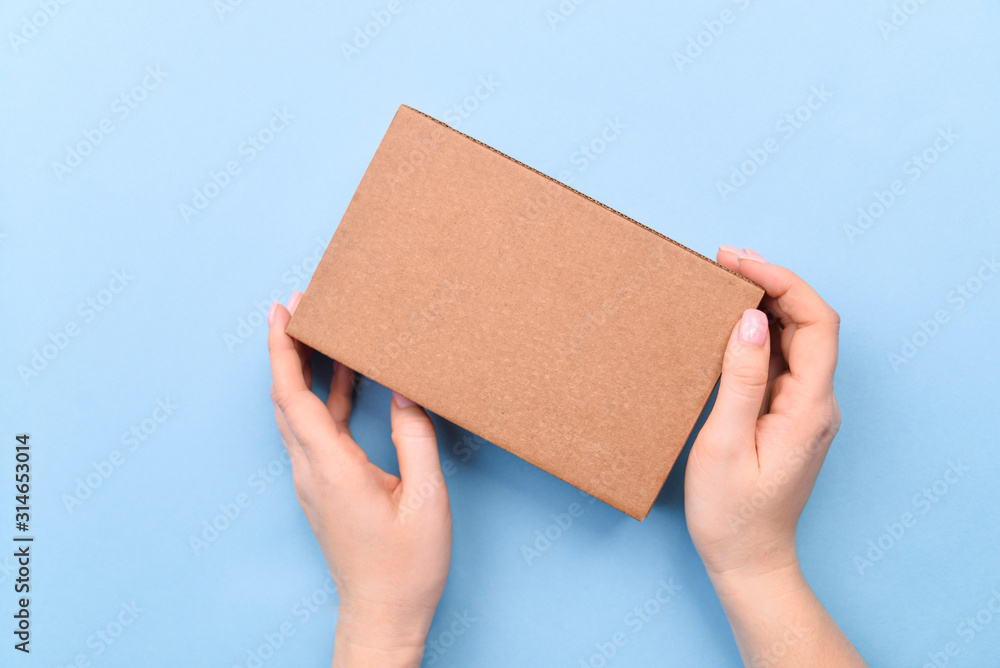 Hands holding craft paper gift box with as a present for Christmas, new year, valentine day or anniversary on blue background, top view Hands holding craft paper gift box with as a present for Christmas, new year, valentine day or anniversary on blue background, top view