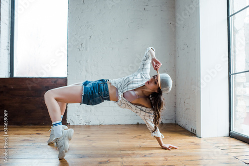 attractive girl touching cap while dancing hip-hop in dance studio