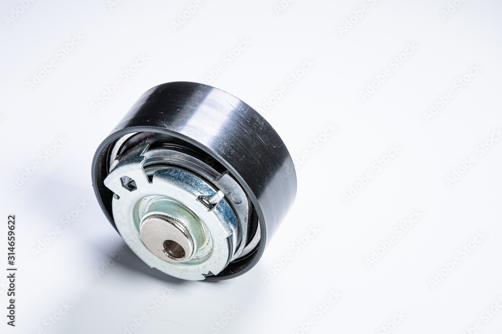 Tension roller of a timing belt of an internal combustion engine on a gray background. The concept of new spare parts and maintenance of vehicles Tension roller of a timing belt of an internal combustion engine on a gray background. The concept of new spare parts and maintenance of vehicles
