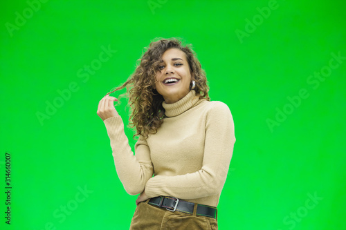 Alluring sensual young lady rolling a lock of her curly hair around her finger, smiling, looking happy and coquettish. © Andrii