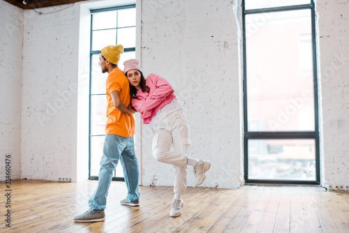 attractive dancer posing while standing with crossed arms near african american man