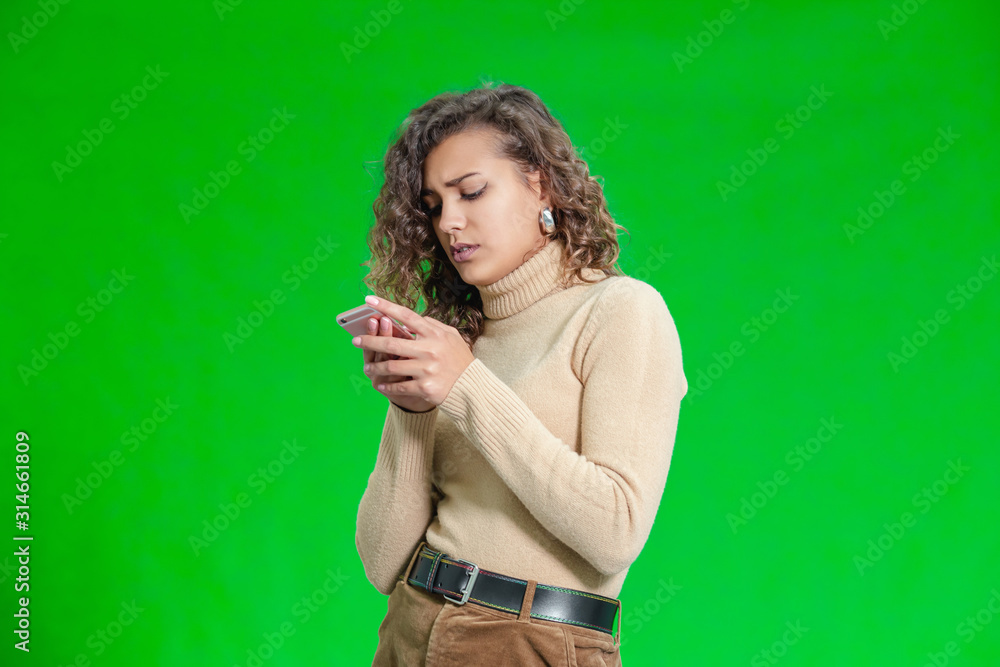 © Andrii - Portrait of anxious and puzzled girl looking at smartphone screen, being worried, standing over gren background. © Andrii - Portrait of anxious and puzzled girl looking at smartphone screen, being worried, standing over gren background.