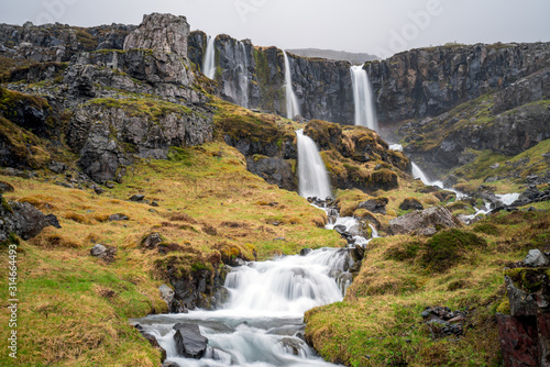 A waterfall cascade in Mjoifjordur in East Iceland near Klifbrekkufossar. Foggy and rainy weather. Longe exposure shot. Landscape, scenery and traveling concept. photo