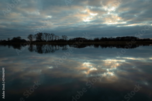 Reflection of clouds in calm water  trees on the horizon  evening view