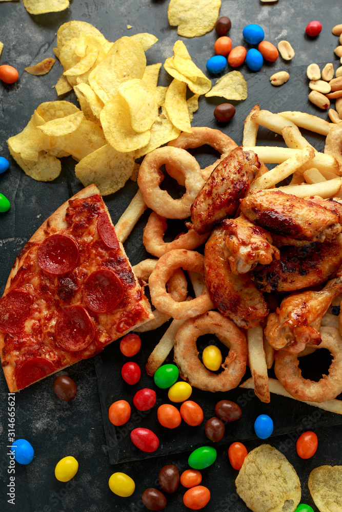 Unhealthy, Fast food concept. onion rings, pizza, french fries, bbq chicken, candy, chocolate, potato chips, salt peanuts. Unhealthy, Fast food concept. onion rings, pizza, french fries, bbq chicken, candy, chocolate, potato chips, salt peanuts.