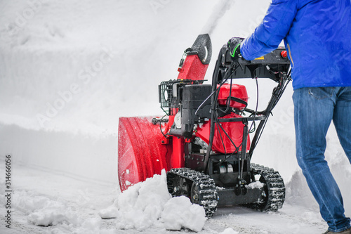 Man clearing or removing snow with a snowblower on a snowy road detail. photo