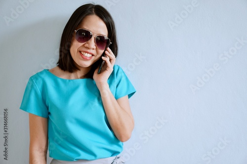 A young beautiful asian woman wearing sunglasses and turquoise color blouse using a black smart phone