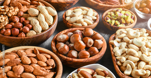 A variety of nuts in wooden bowls from top view. Walnuts, cashew, almond, pistachio, pecan, hazelnut, macadamia and peanut mix selection. Healthy fitness super food banner or panorama.