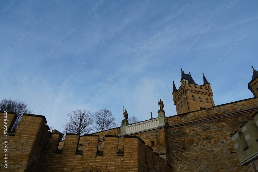 external fortifications or walls of the Hohenzollern Castle in Bisingen Germany. There are tower and  entrance with two statues displayed, the photo is taken in upper view. 