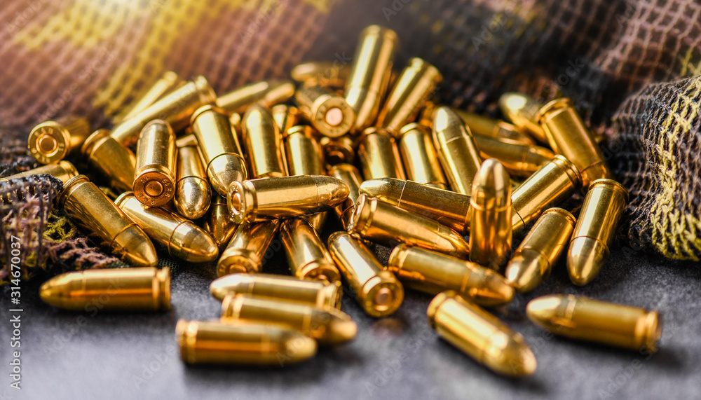 Pile of fire bullets or ammunition on dark stone table. Hand guns weapon in background. Many projectiles into 9mm gun. Pile of fire bullets or ammunition on dark stone table. Hand guns weapon in background. Many projectiles into 9mm gun.
