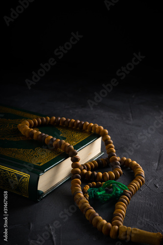 Faith in Islam concept. The Islamic holy book, Quran or Kuran, with rosary beads or “tasbih” on dark background.