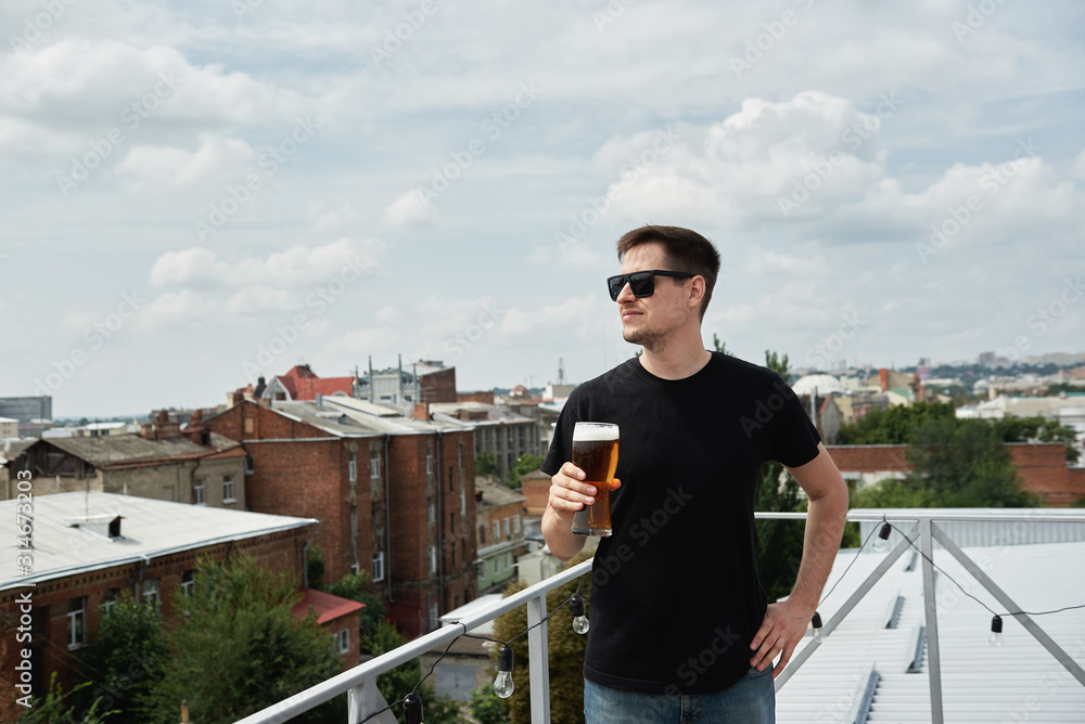 Happy man in black shirt and eyewear drinking beer at bar or pub on roof, copy space Happy man in black shirt and eyewear drinking beer at bar or pub on roof, copy space