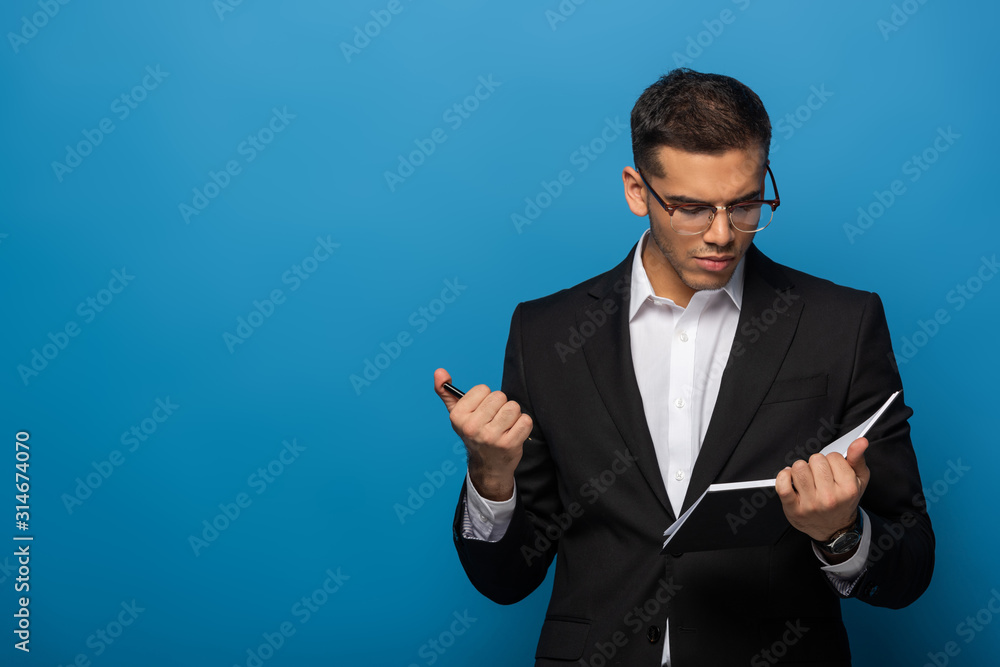 Young businessman holding pen and looking at copy book on blue background Young businessman holding pen and looking at copy book on blue background