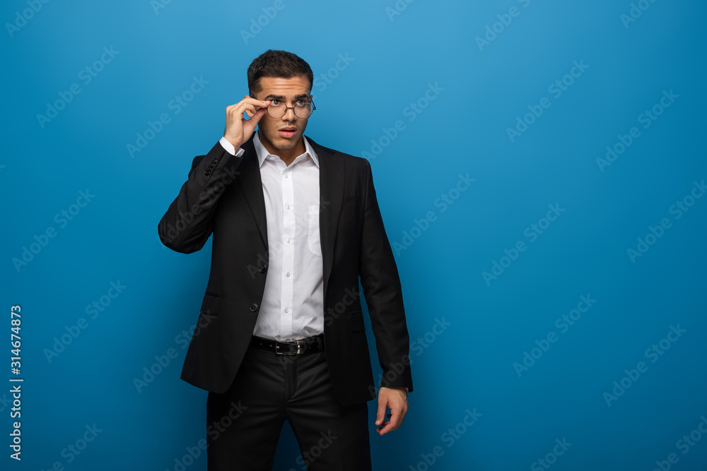 Handsome businessman adjusting eyeglasses and looking away on blue background Handsome businessman adjusting eyeglasses and looking away on blue background